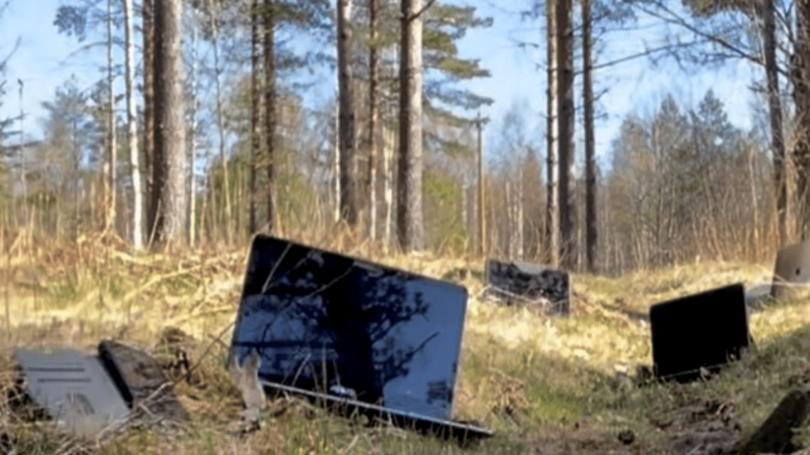 Syksyinen metsämaisema, jossa etualalle maahan on ripoteltu useita kannettavia tietokoneita. Etumaisen tietokoneen ruudulta heijastuu puiden oksia.