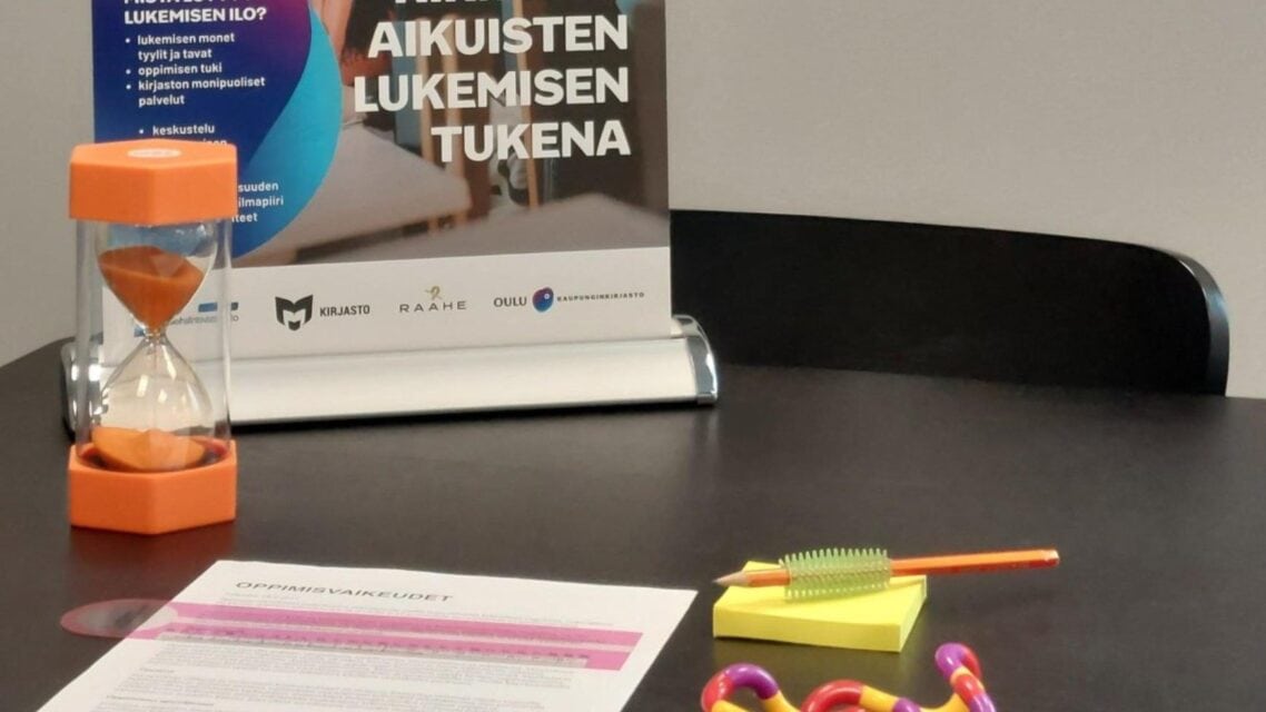 Tummalle pöydälle on aseteltu tiimalasi, tangle, lyijykynä kynänpidikkeineen sekä paperi, jonka päällä on vaaleanpunasävyinen lukuviivain.